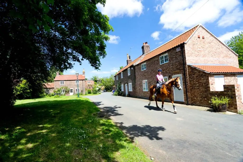 A woman riding a horse past the Tailors Cottage in picturesque Lund, East Riding of Yorkshire.